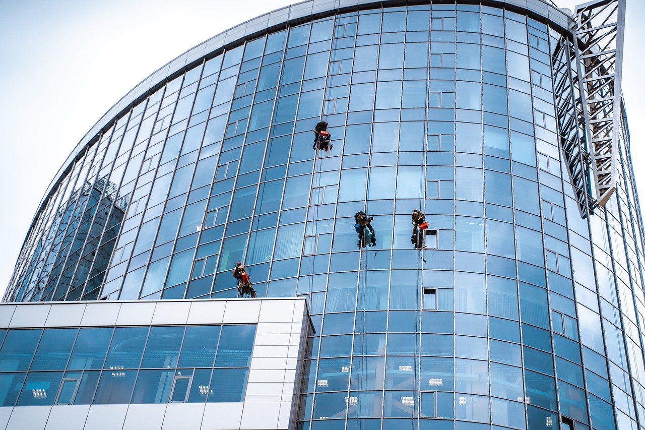 window cleaning, modern architecture, glass building, skyscraper construction, building maintenance, high-rise worker, urban landscape, building facade, urban climbing, safety equipment, rope work, cleanliness, workwear, weather conditions, outdoor work, access systems, tall buildings, architectural design, office building, blue glass